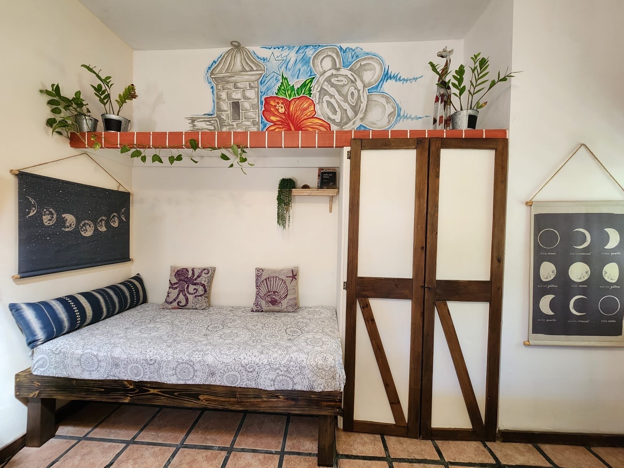 Una habitación acogedora con una cama, un mural y una planta colgante.