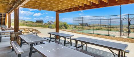 An outdoor patio with picnic tables and benches, a stone wall, and a view of houses and a fenced area.