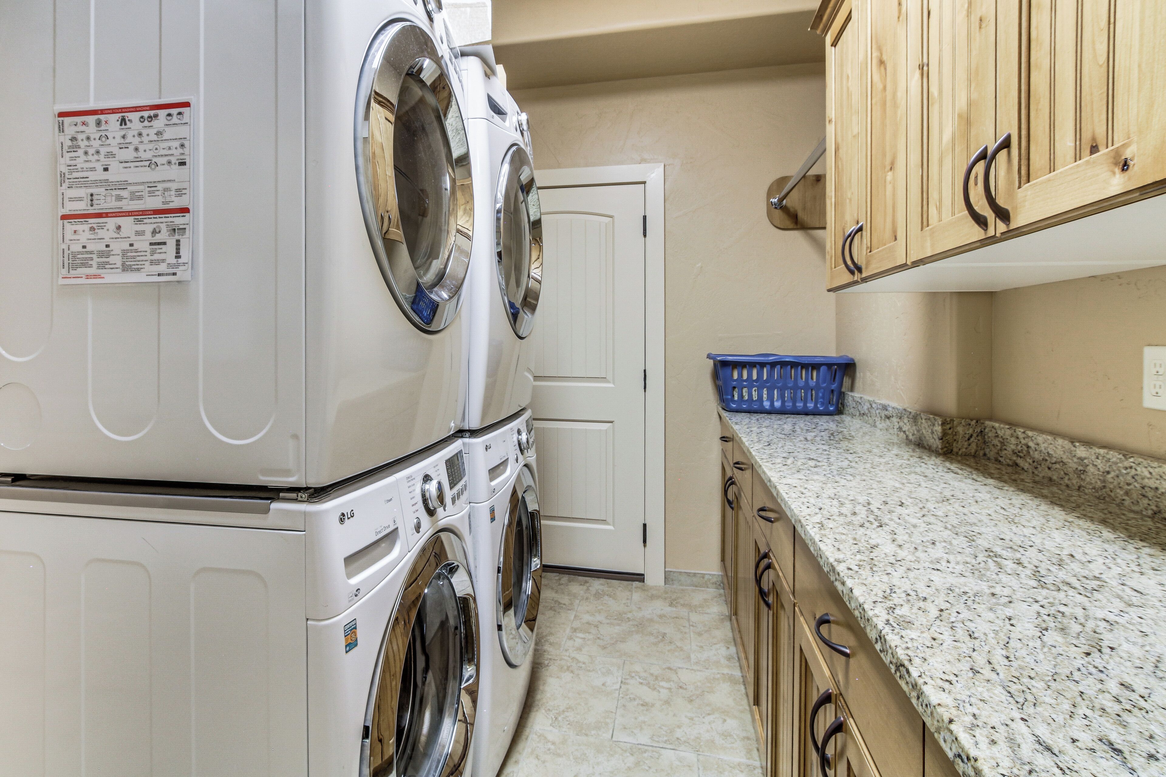 A laundry room with stacked washers and dryers, a door, a blue laundry basket, and wooden cabinets.