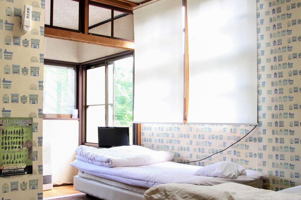 A room with a bed, a television, and a window with a blind.