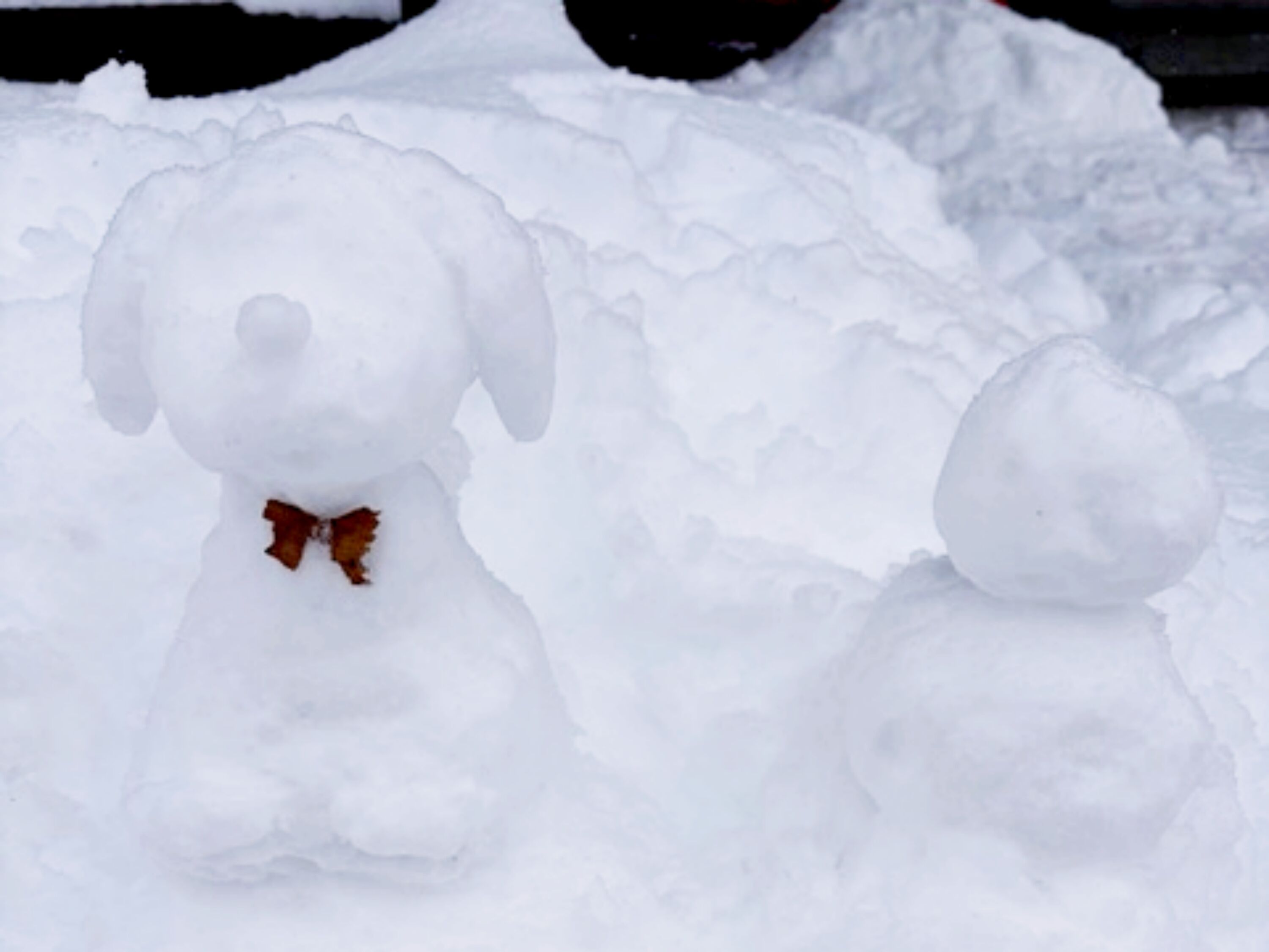 A snowman with a bow tie and a smaller snowball next to it.