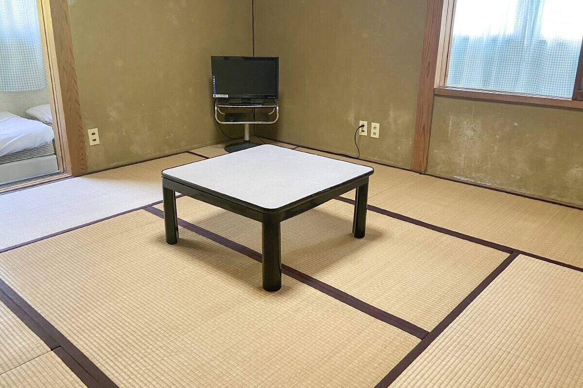 A tatami mat room with a small table and a television on a stand.