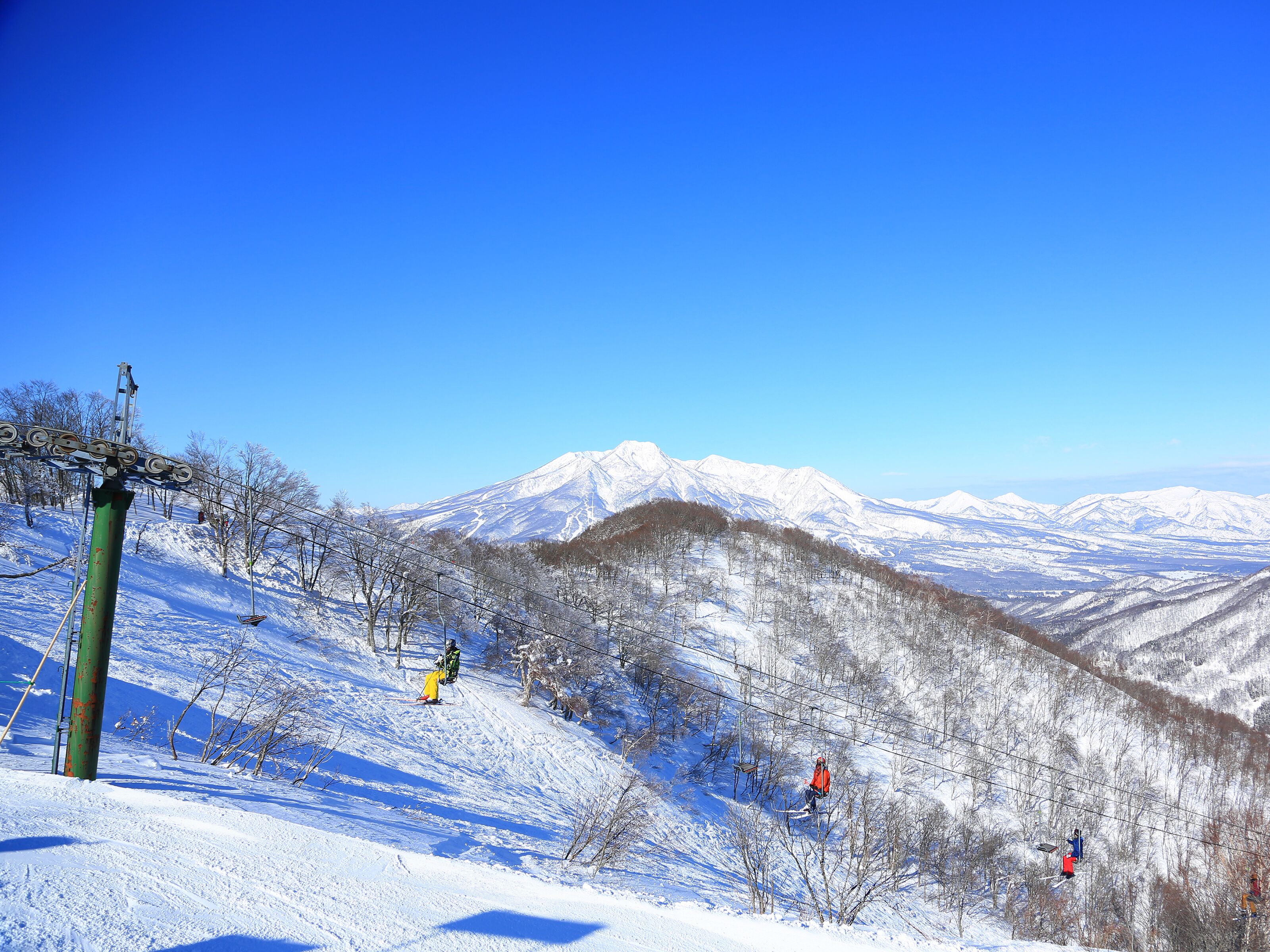 Paesaggio montano innevato con impianti di risalita e sciatori.