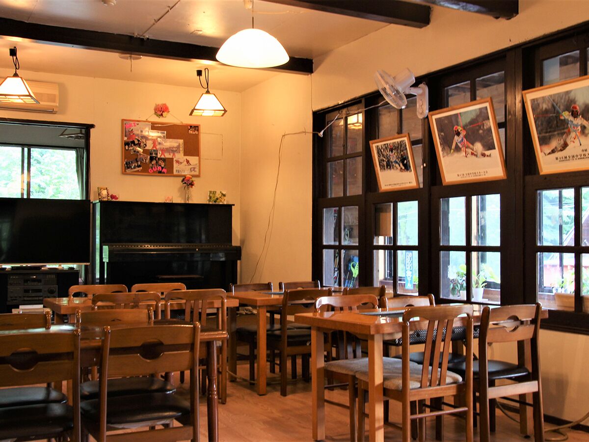Un espace repas avec des tables et des chaises en bois, un tableau noir et des tableaux encadrés accrochés au mur.