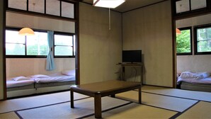Una habitación japonesa tradicional con suelo de tatami, una mesa de madera baja y un televisor sobre un soporte.