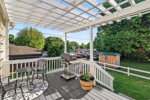 Eine überdachte Terrasse im Freien mit Grill, Stühlen und einem Blumentopf.