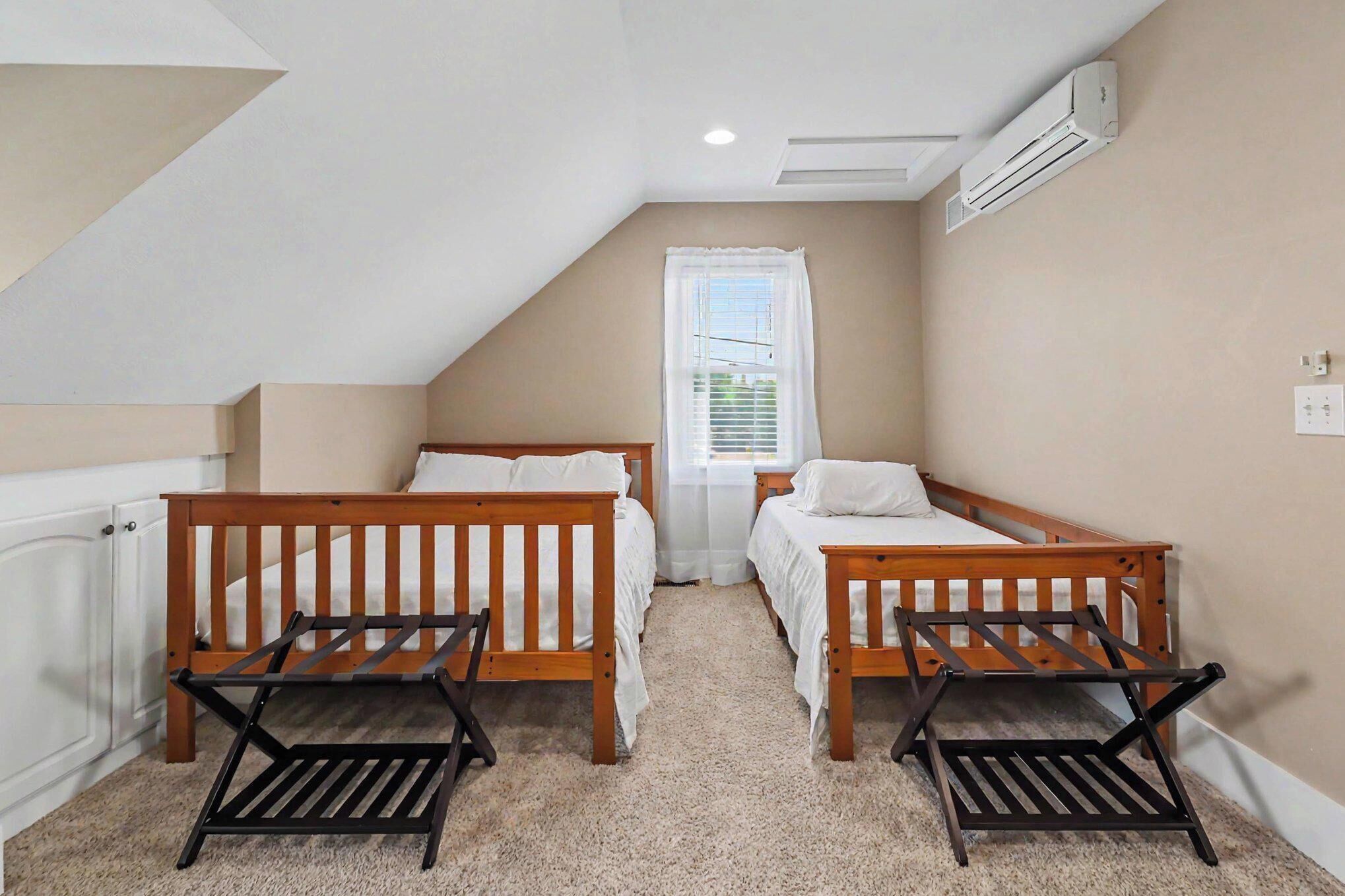 A bedroom with two wooden beds, a window with white curtains, a radiator, and a ceiling fan.