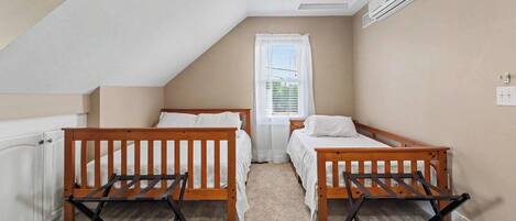 A bedroom with two wooden beds, a window with white curtains, a radiator, and a ceiling fan.