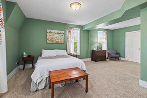 Ein Schlafzimmer mit Bett, Nachttischen, Kommode, Stuhl und einem fenster mit Vorhängen.