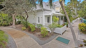 A single-story house with a porch, surrounded by a variety of plants and trees.