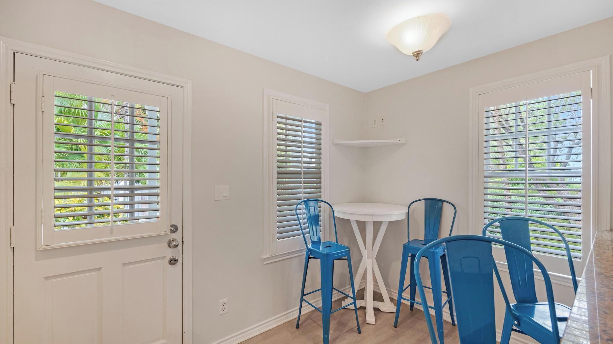 A room with two white doors, a white ceiling fan, and a small white table with blue chairs.