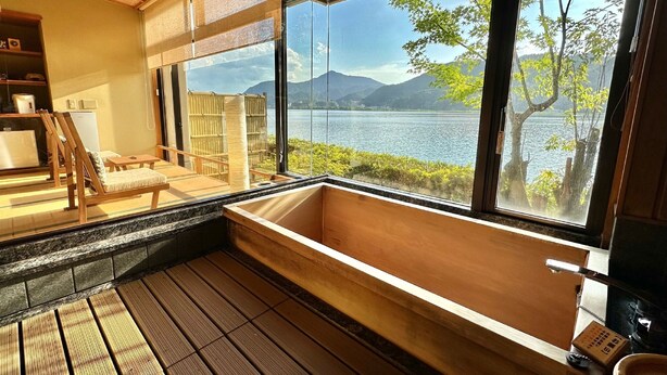 Quarto em estilo japonês tradicional com piso de madeira, banheira de madeira e vista para um lago com montanhas ao fundo.