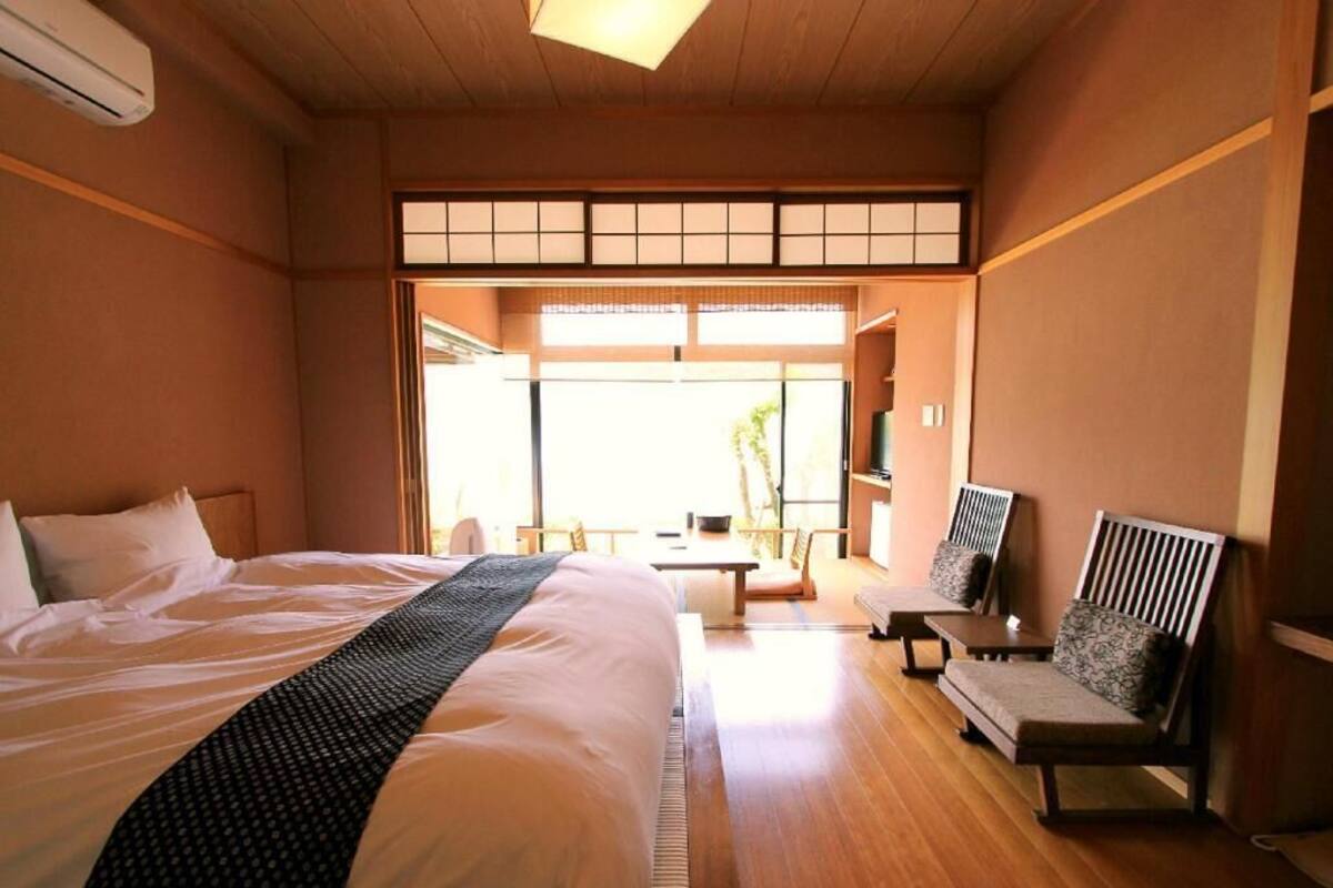 A hotel room with a large bed, a seating area with a sofa and chairs, a television, and a sliding door leading to a balcony.