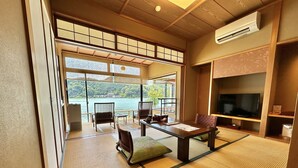 Quarto japonês tradicional com tatames, uma mesa baixa, cadeiras e uma televisão.
