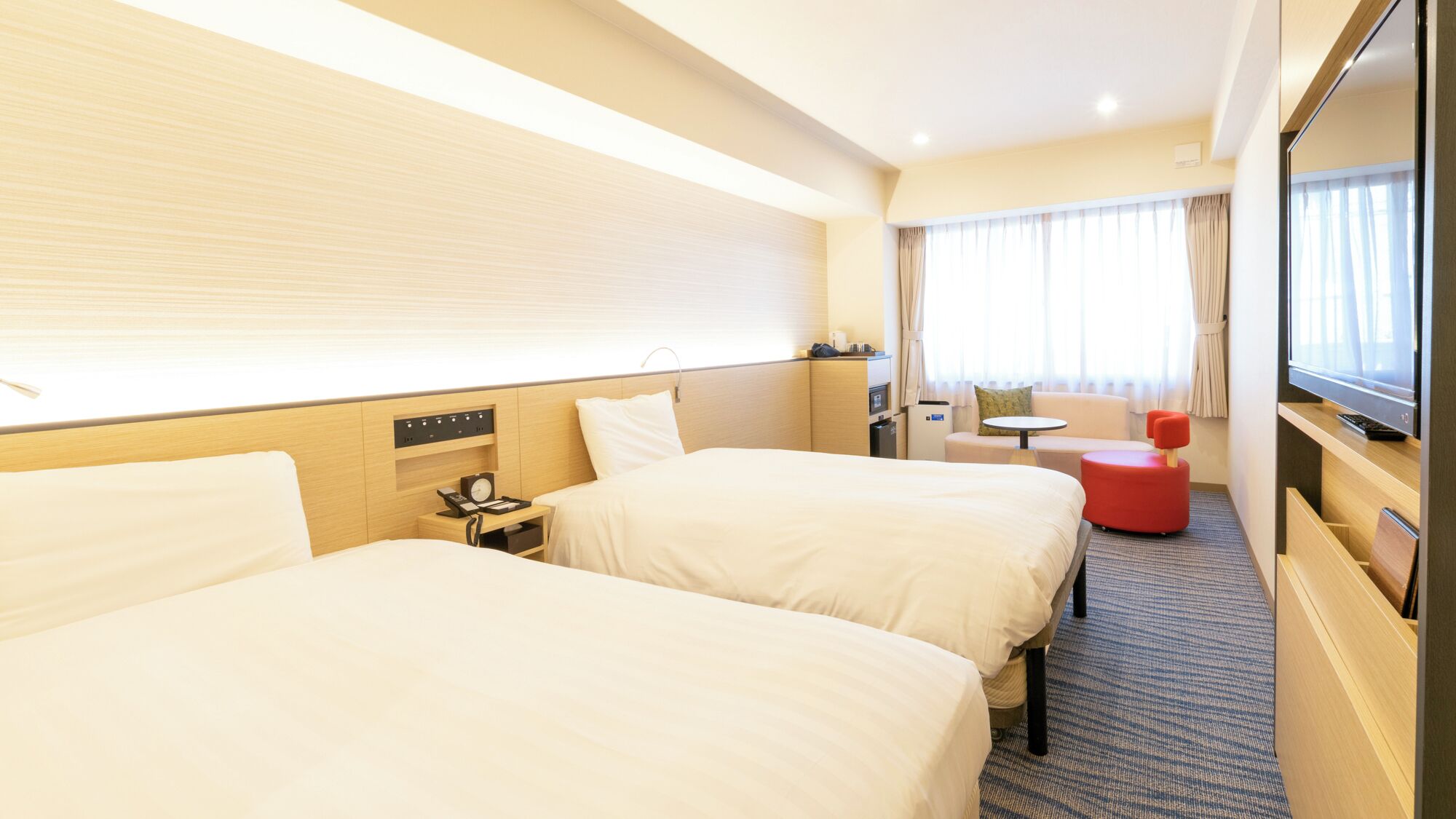 A hotel room with two beds, a desk, a chair, a TV, and a window with curtains.
