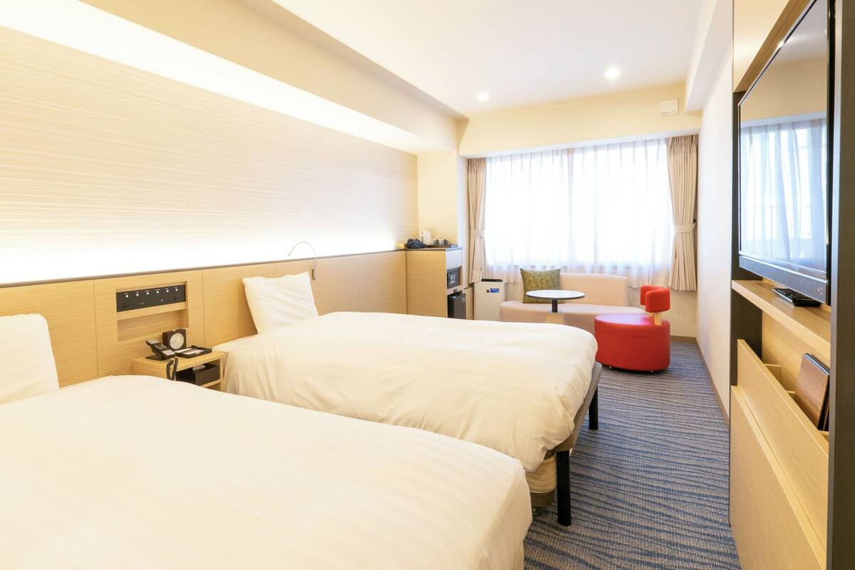 A hotel room with two beds, a desk, a chair, a TV, and a window with curtains.