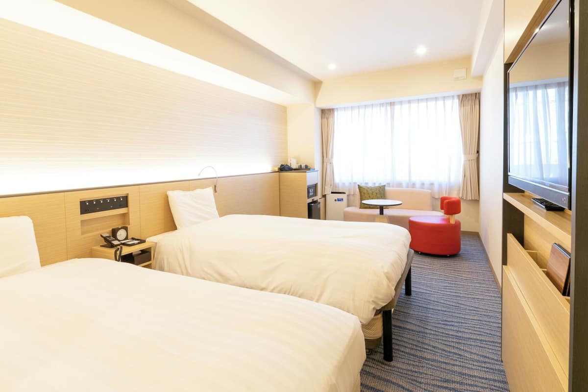 Une chambre d’hôtel avec deux lits, un bureau, une chaise, une télévision et une fenêtre avec des rideaux.