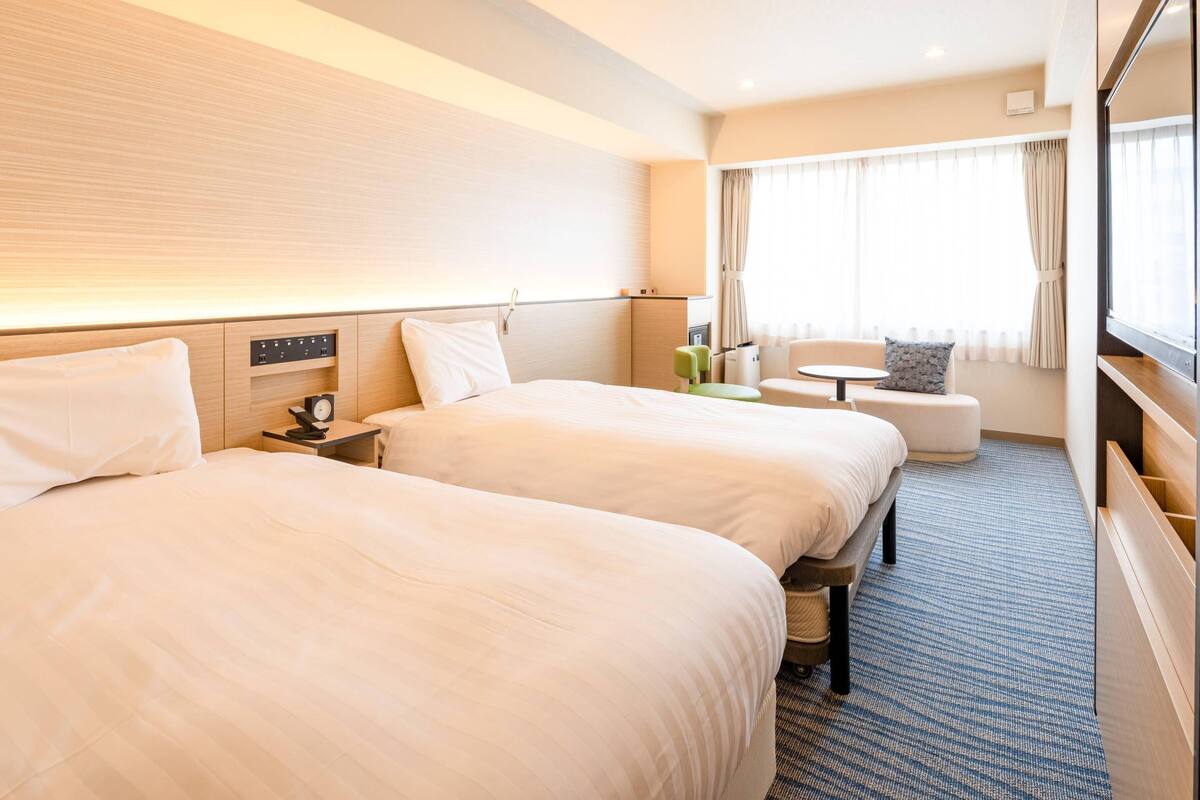 A hotel room with two beds, a small table, a chair, and a TV.