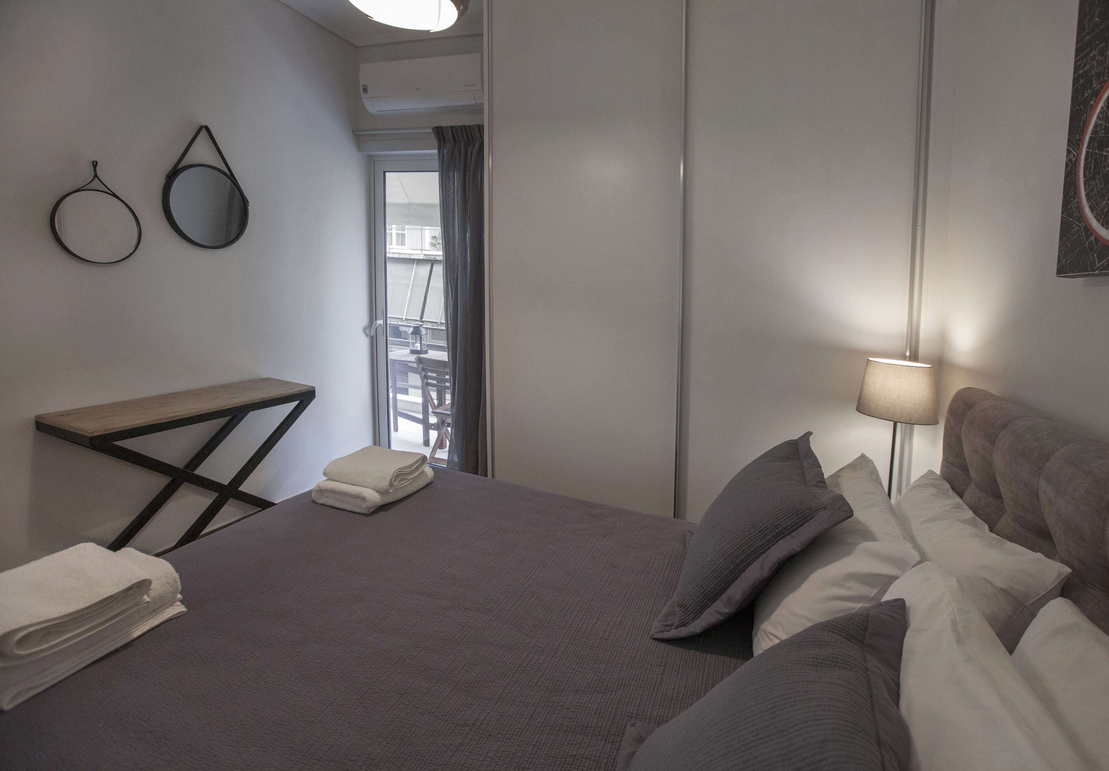 Quarto de hotel com uma cama, mesa de cabeceira com abajur, espelho e vista para o exterior.