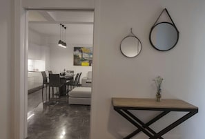 A modern kitchen with white cabinets, a dining area with a white table and chairs, and a hallway with a wooden console table and two wall-mounted mirrors. - Unique Apartment near Acropolis by GHH (Athens)