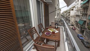 A balcony with wooden furniture, a table with a bowl of grapes and a glass of wine, and a view of the street below. - Unique Apartment near Acropolis by GHH (Athens)