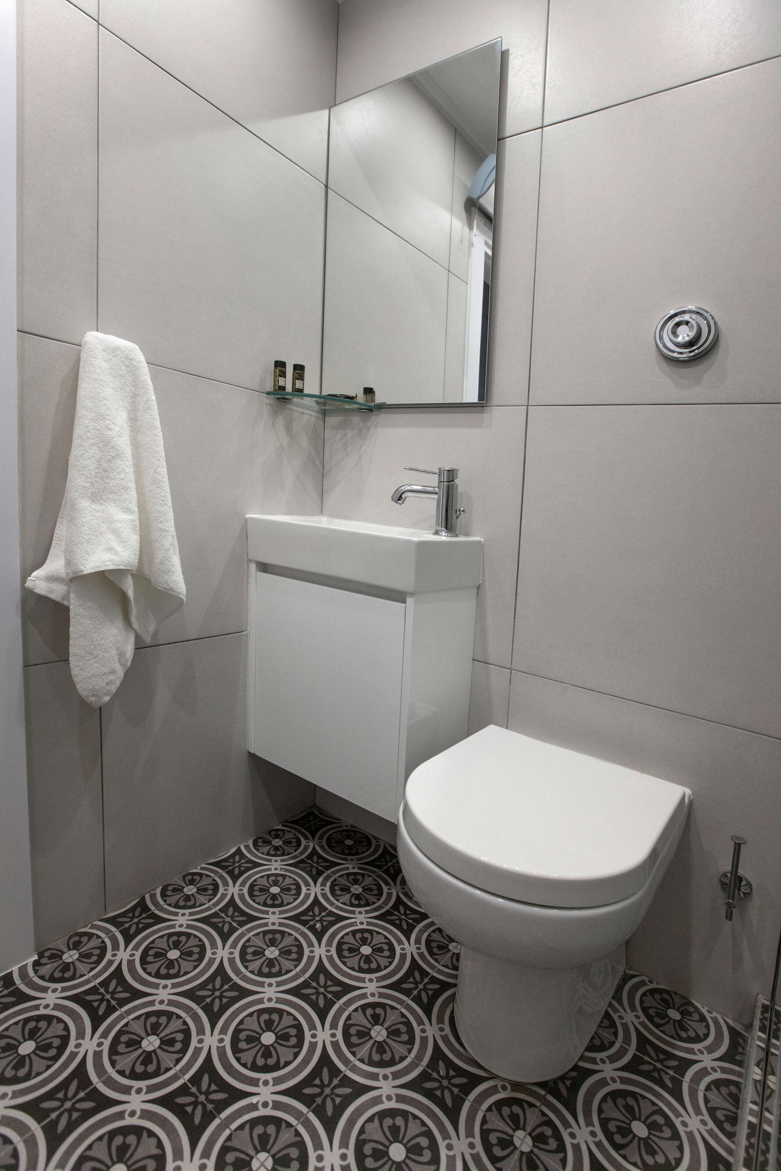Un baño con inodoro, lavabo, espejo y baldosas de suelo estampadas.