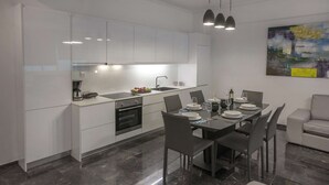 A modern kitchen with white cabinets, a dining area with a table set for four, and a gray sofa. - Unique Apartment near Acropolis by GHH (Athens)