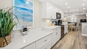 A modern kitchen with white cabinetry, a large island, and a dining area with a table and chairs. - Island House Beach Resort 14N (Siesta Key)