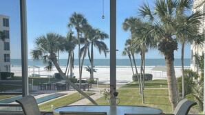 A view from a balcony with a table and chairs, overlooking a beach with palm trees and a pool. - Island House Beach Resort 14N (Siesta Key)