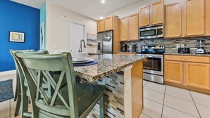 Una cocina con armarios de madera, electrodomésticos de acero inoxidable y encimera de granito, junto con una zona de comedor con sillas.