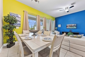 A dining area with a table set for four, a ceiling fan, and a large window with curtains. - Bright 3B/2.5B townhome at Enclaves at Festival, minutes from Disney & Champions Gate. Private pool, resort amenities, sleeps 8. (Davenport)