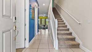 Un pasillo con una escalera, una puerta con picaporte moderno y un ventilador de techo.