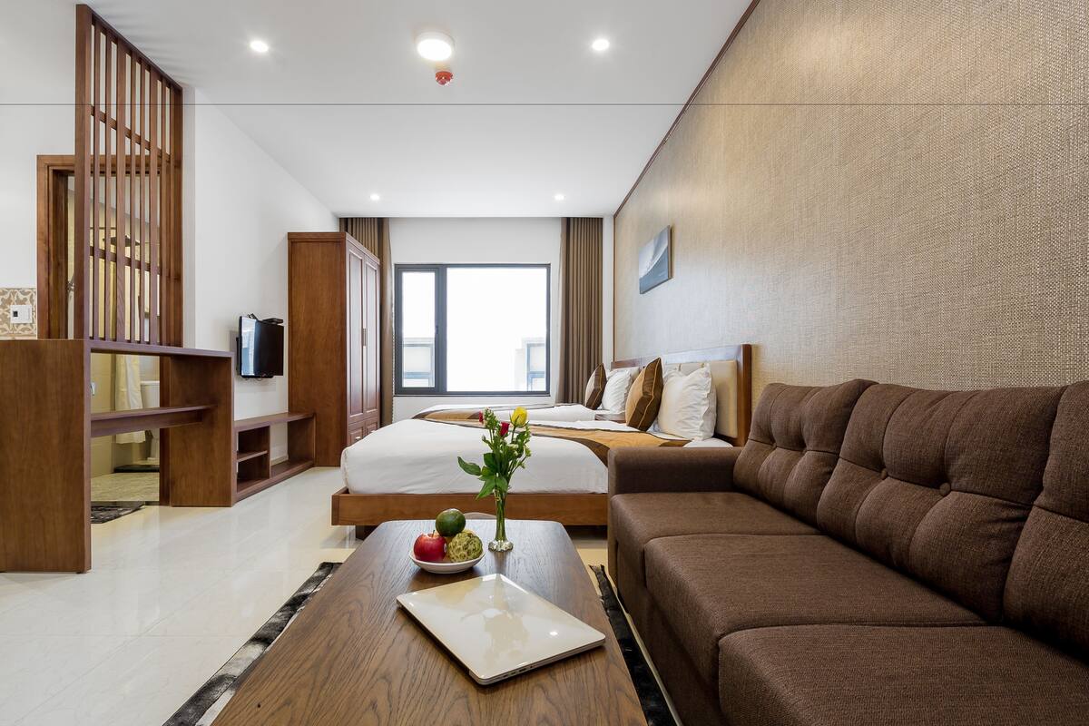 Une chambre d’hôtel moderne avec un grand lit, un canapé marron, un bureau en bois et une télévision.
