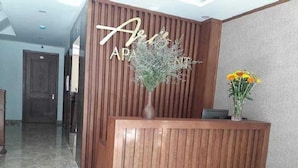 Un mostrador de recepción con acabado de madera, una planta en maceta y un florero con flores.