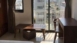 Una habitación de hotel moderna con una cama grande, un escritorio pequeño, una silla y un balcón con vista a la ciudad.