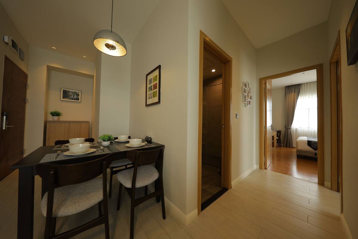 Un comedor con una mesa lista para dos personas, una lámpara colgante y un cuadro en la pared.