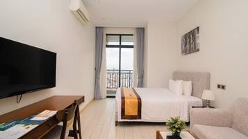A hotel room with a bed, a desk with a chair, a television, and a balcony with curtains.