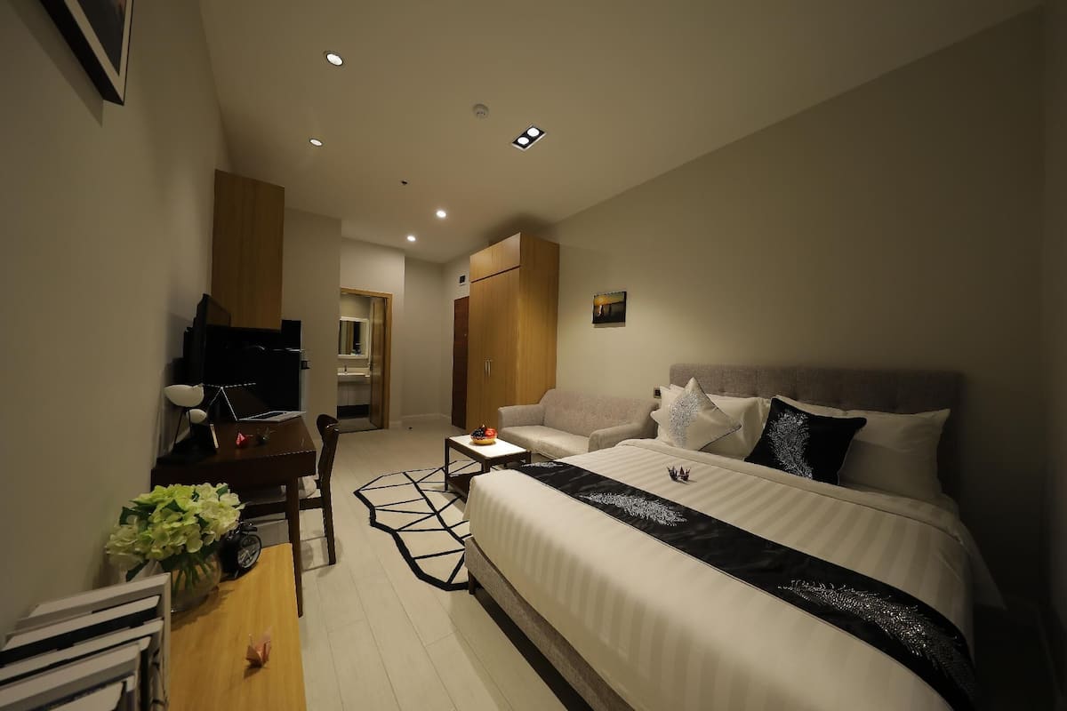 Una habitación de hotel moderna con una cama grande, un escritorio con silla, una mesita de noche con lámpara y un jarrón decorativo.
