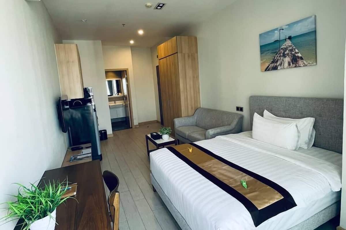Una habitación de hotel moderna con cama, escritorio, silla, sofá y un cuadro en la pared.