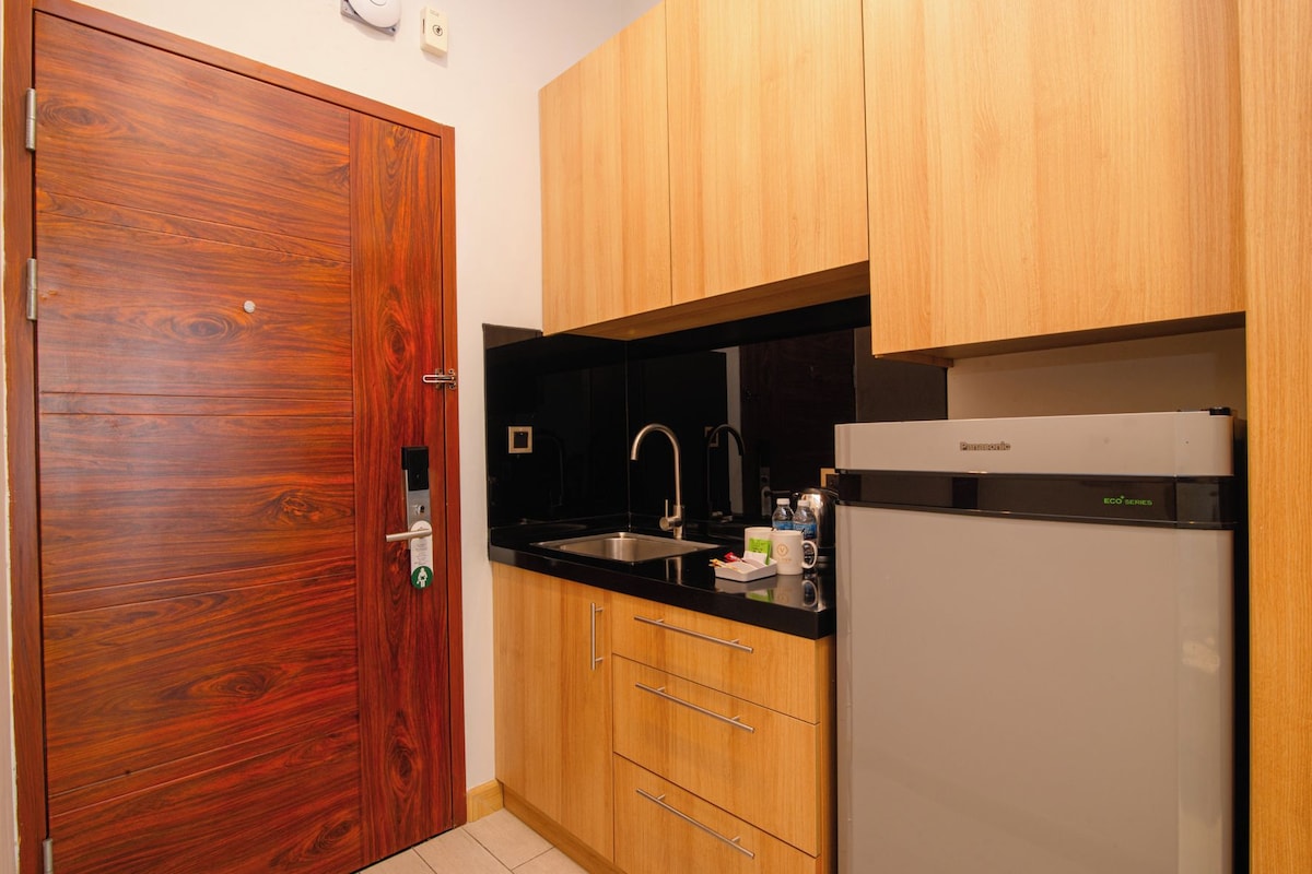 A compact kitchen with wooden cabinets, a black countertop, a stainless steel sink, and a white refrigerator.