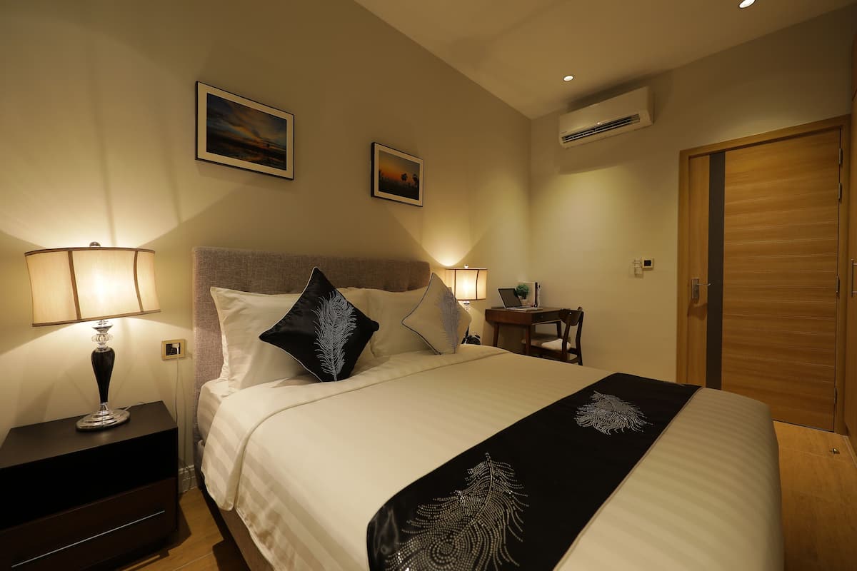 Habitación de hotel ordenada con cama, lámparas de noche, una mesita con lámpara y aire acondicionado de pared.