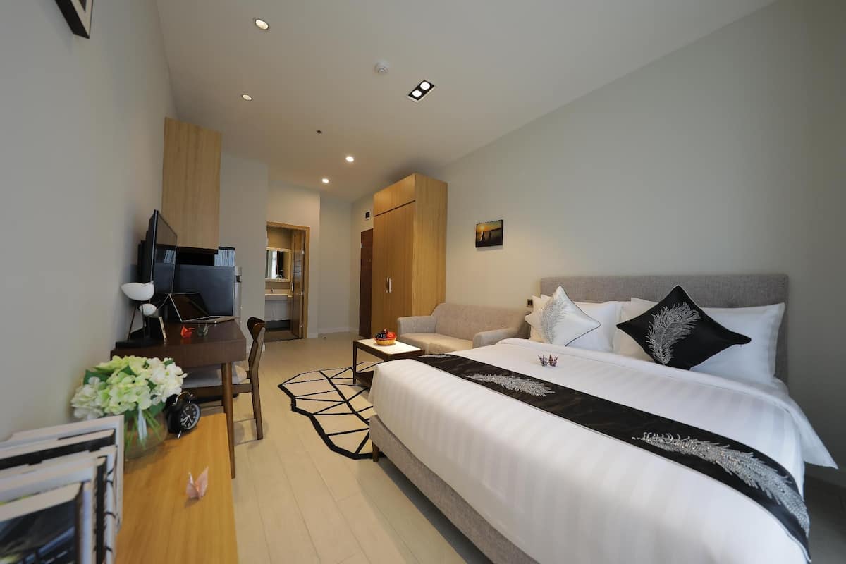 Habitación de hotel moderna con una cama grande, un escritorio con computadora, una mesita con un florero y un armario.