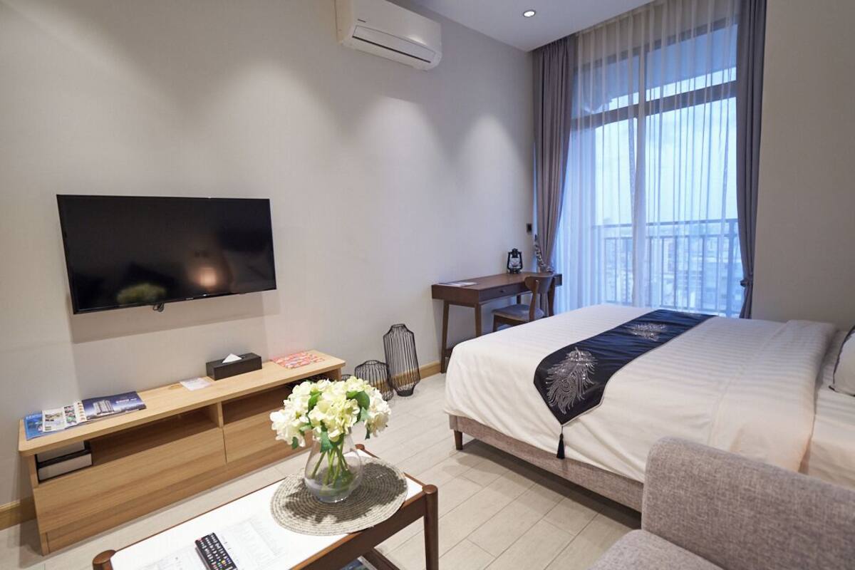 Habitación de hotel con televisión, escritorio, cama, silla y un florero con flores.