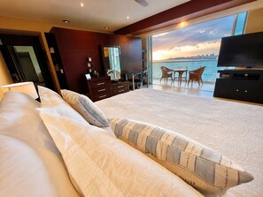 A hotel room with a large bed, a TV, a desk, and a balcony with a city view. - Gather your loved ones and pack your bags for the vacation of a life time!  (Puerto Vallarta)