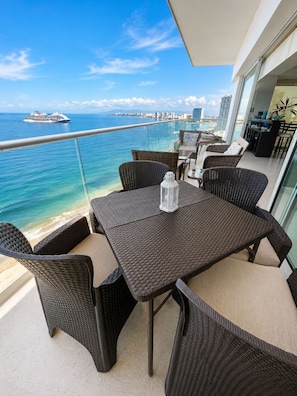 A balcony with wicker furniture, a table, and a view of the ocean and a cruise ship. - Gather your loved ones and pack your bags for the vacation of a life time!  (Puerto Vallarta)