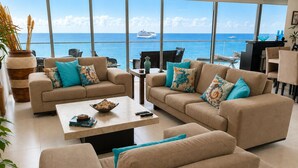Amplia sala de estar con grandes ventanales con vista al mar, que cuenta con dos sofás, una mesa de centro y una mesa de comedor.