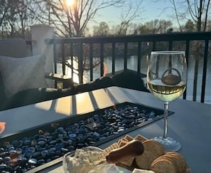Uma mesa com um copo de vinho branco, uma bandeja de mirtilos e pão numa varanda com vista para um corpo de água.