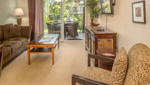 A living room with a sofa, a coffee table, a chair, a TV mounted on the wall, and a view of the outside balcony.