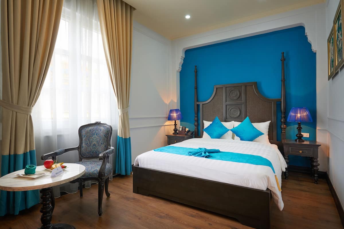 Een hotelkamer met een groot bed, een stoel, een klein tafeltje en een nachtkastje met lampen.