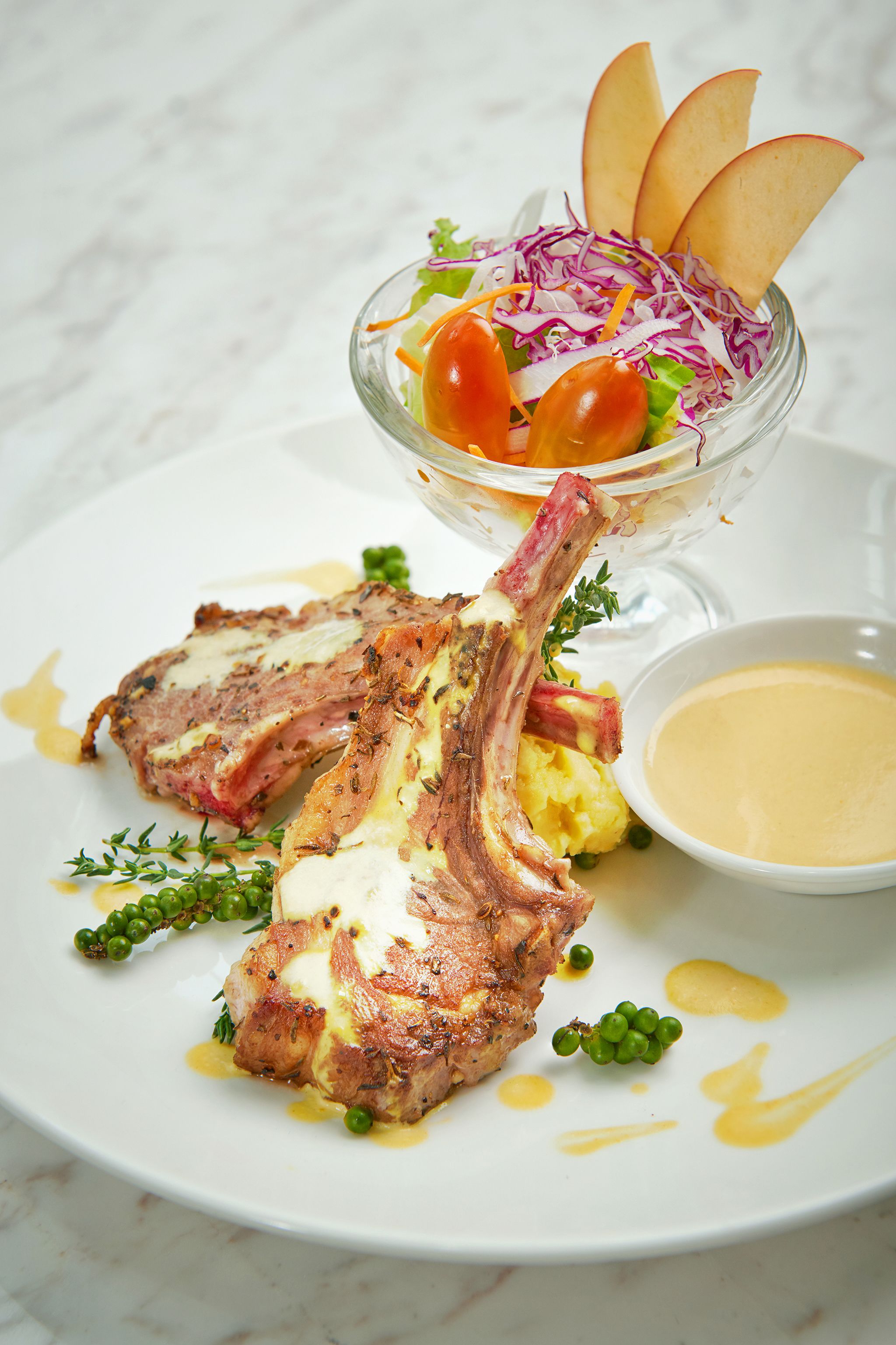 Un plato con chuletas de cordero, una ensalada y un bol de salsa.